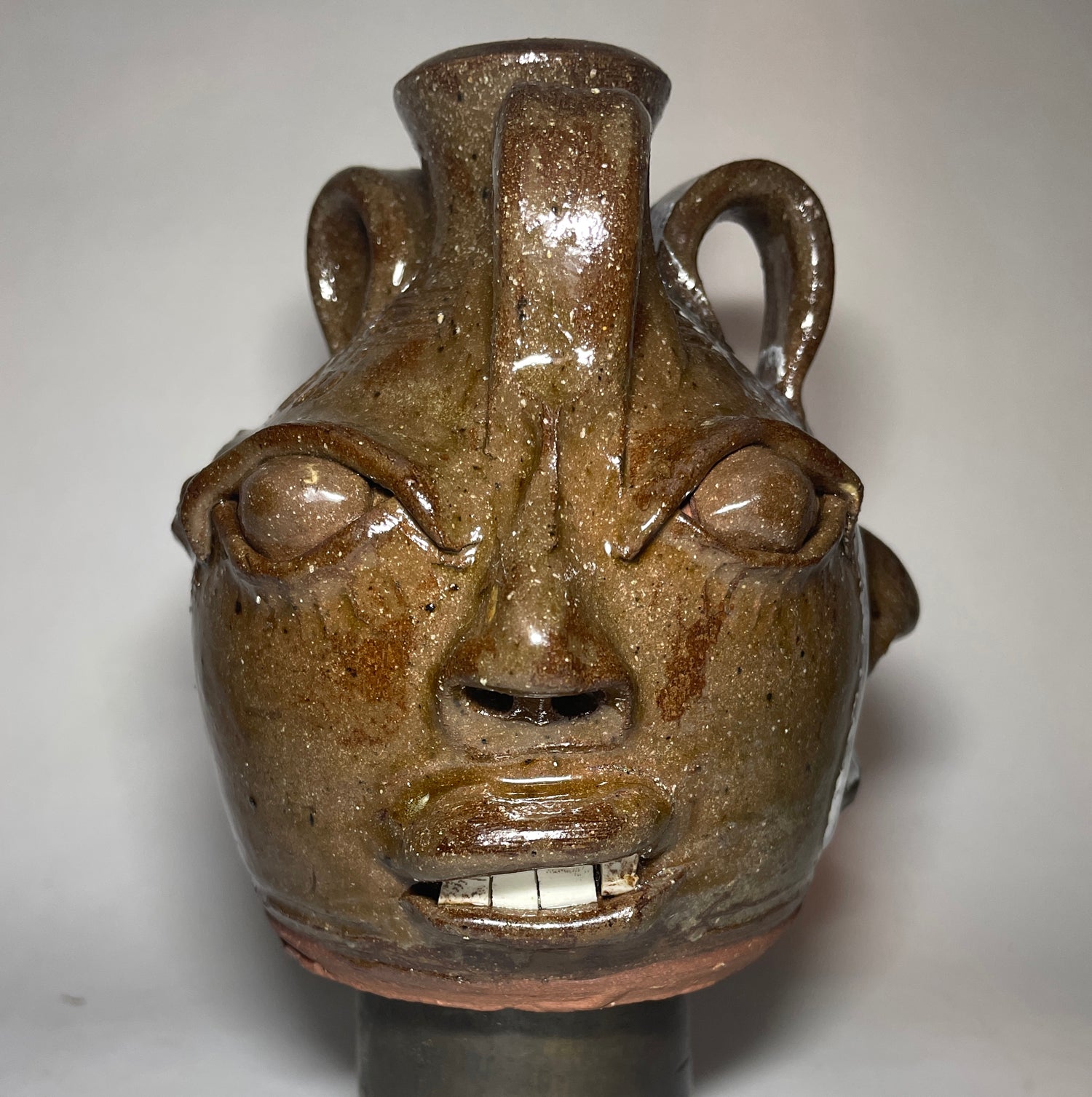 Face 1 of triple face jug.  Brown clay, clear glaze.  Broken china plate teeth.