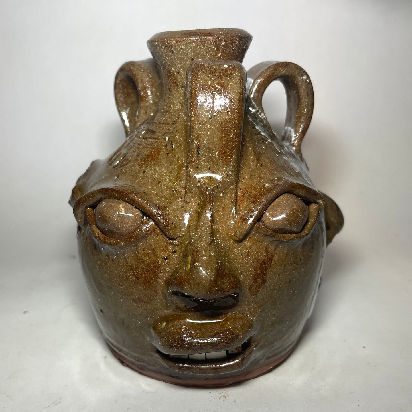 Face 1 of triple face jug.  Brown clay, clear glaze.  Broken china plate teeth.