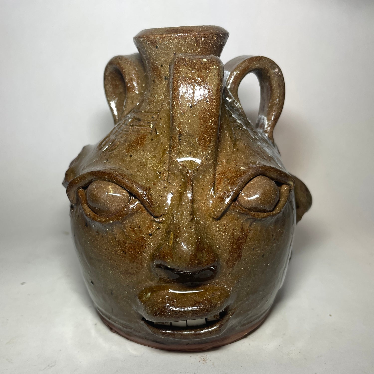 Face 1 of triple face jug.  Brown clay, clear glaze.  Broken china plate teeth.