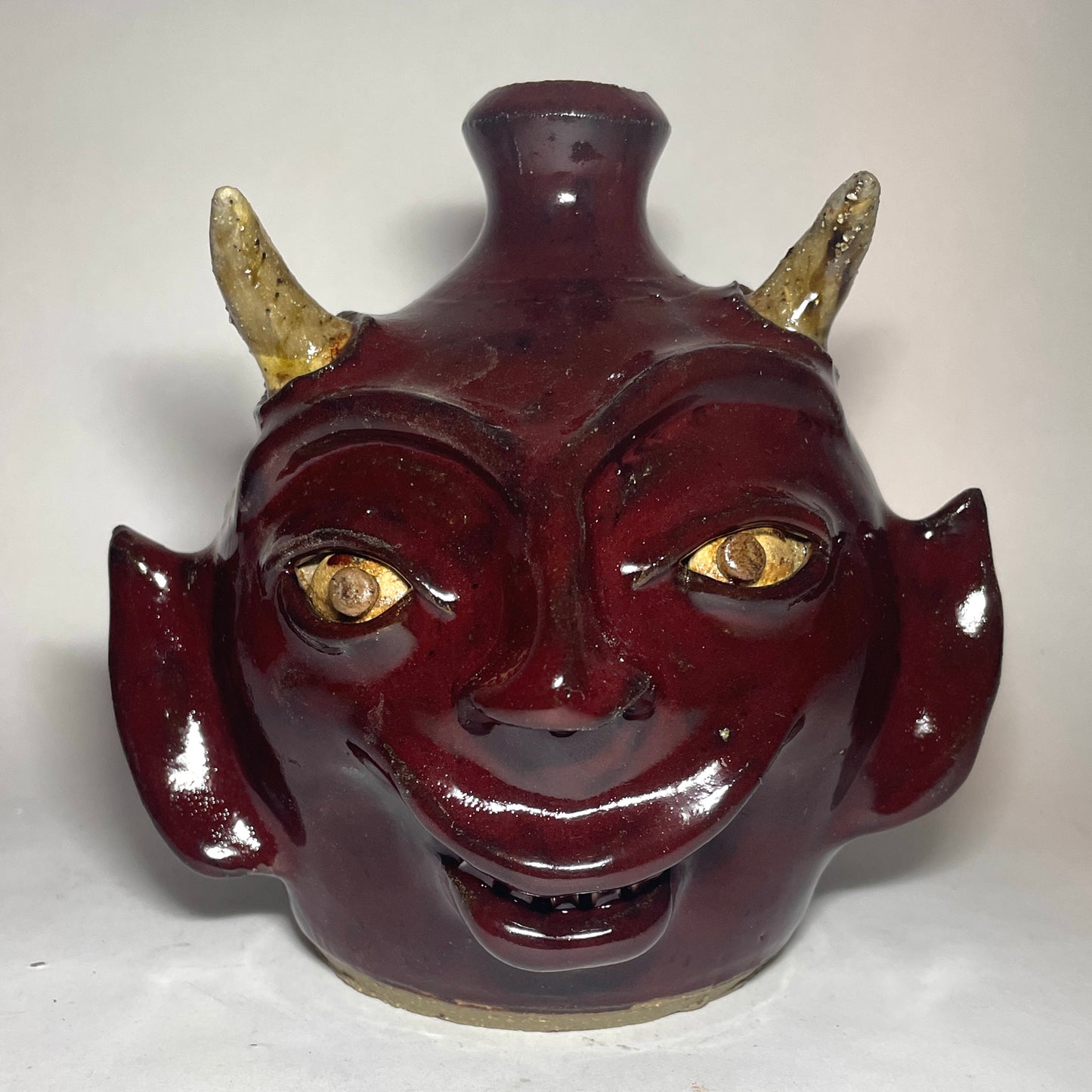 Devil face jug with red glaze, two horns, and broken china plate teeth.
